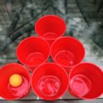 Top view of red plastic cups with a yellow ping pong ball, outdoors.